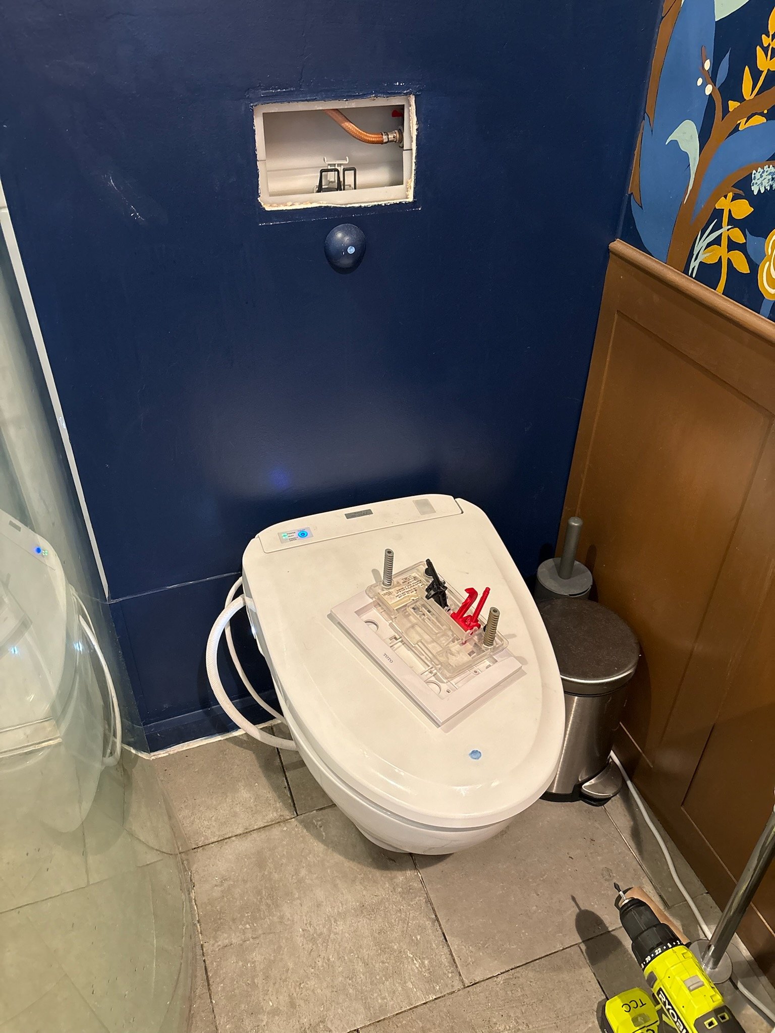 Access opening to a concealed toilet tank above a wall-hung toilet during service