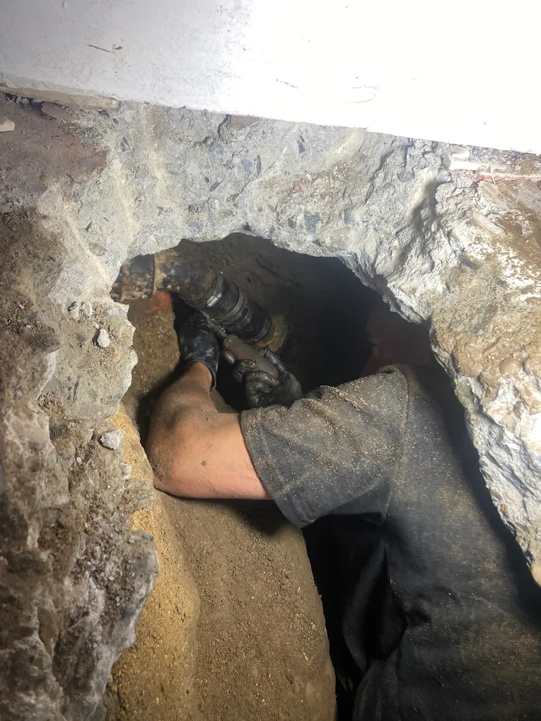 Technician working on exposed drain piping near a concrete floor
