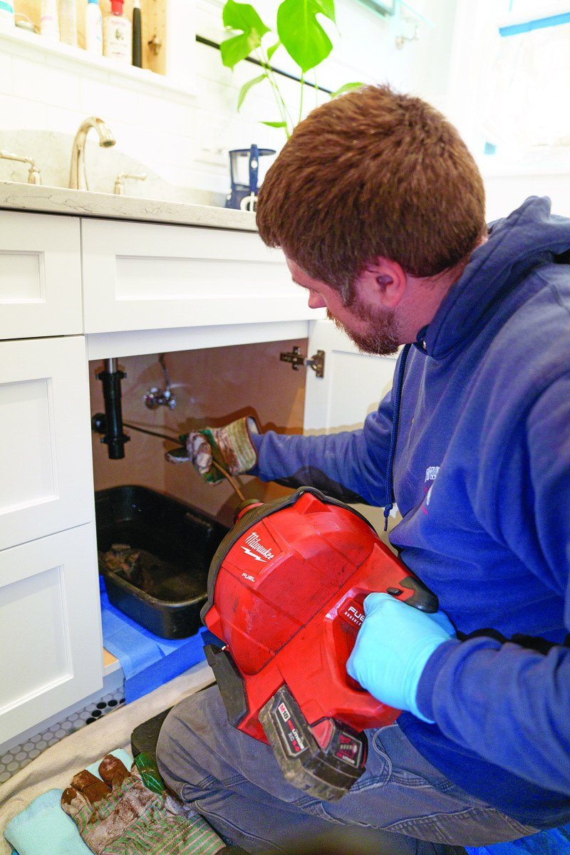 Plumber feeding a drain cable into kitchen sink piping with the P-trap removed